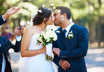 Image showing Happy bride and groom sharing a kiss while surrounded by guests and being showered with confetti rose petals after wedding ceremony