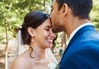 Image showing Beautiful young couple on their wedding day. Groom kissing his joyful bride on the forehead while they stand together on a sunny day
