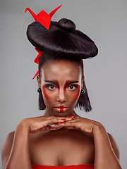 Image showing What is makeup but fashion for your face. Studio shot of a beautiful young woman wearing Asian inspired makeup and posing with origami against a grey background.