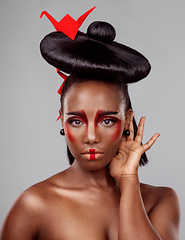 Image showing Whatever your look, wear it like you mean it. Studio shot of a beautiful young woman wearing Asian inspired makeup and posing with origami against a grey background.