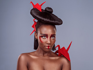 Image showing Africa meets Asia. Studio shot of a beautiful young woman wearing Asian inspired makeup and posing with origami against a grey background.