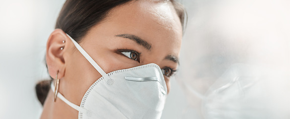 Image showing Where do you go when the walls are closing in. a masked young businesswoman looking thoughtfully out of a window in a modern office.