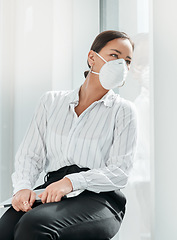 Image showing Will business ever be the same again. a masked young businesswoman looking out of a window in a modern office.