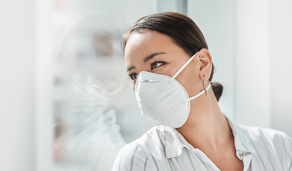 Image showing Clients arent easy to come by these days. a masked young businesswoman looking thoughtfully out of a window in a modern office.