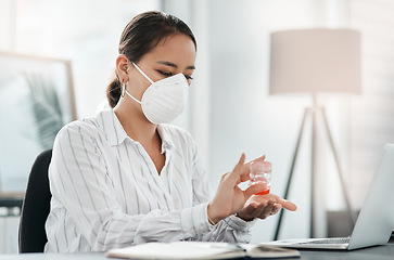 Image showing Lets get to work, but first hand sanitiser. a masked young businesswoman using hand sanitiser while working at her desk in a modern office.