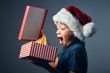 Image showing There is a Santa. Studio shot of a cute little boy opening a Christmas present against a grey background.