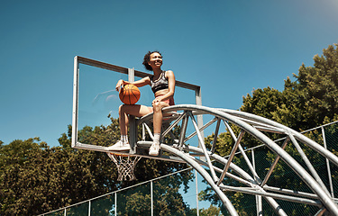 Image showing Do you have what it takes to become the best. a sporty young woman sitting on a basketball hoop on a sports court.