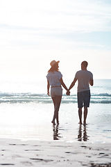 Image showing The beach sets the perfect background to their love. Rearview shot of a young couple walking along the beach.