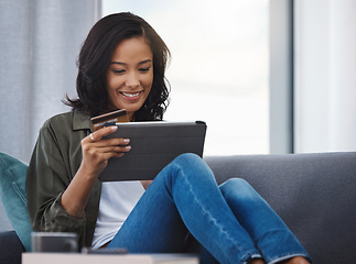 Image showing Who can resist a good bargain. an attractive young woman using a digital tablet and credit card on the sofa at home.