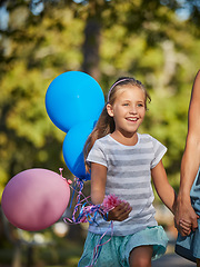 Image showing Best day out ever. an adorable little girl holding balloons and walking in the park with her mother.