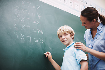 Image showing Shes always there to help. A pretty teacher standing at the blackboard with a young student and helping him with his maths.