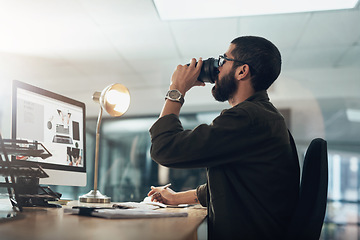 Image showing A bit of coffee keeps him in the game. a young businessman having coffee and using a computer during a late night in a modern office.