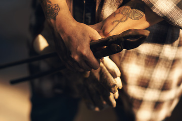 Image showing A blacksmiths hands are her greatest tools. an unrecognisable holding a pair of gloves while working at a foundry.