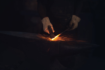 Image showing It might be steel but its worth more than gold. a blacksmith hitting a hot metal rod with a hammer in a foundry.