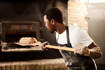 Image showing Support your local baker. a male baker removing freshly baked bread from the oven.