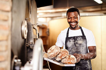 Image showing Now all you need is some butter. a male baker holding up freshly baked bread in his bakery.