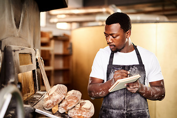 Image showing Lets count how many I just removed from the oven. a male baker making notes while working in his bakery.