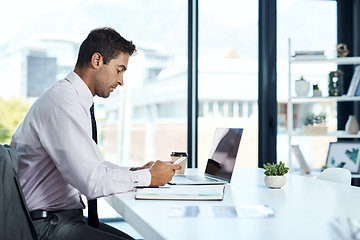 Image showing Keeping everyone up to date. a businessman using his cellphone while sitting at his desk.