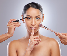 Image showing No one needs to know Im wearing makeup. an attractive young woman posing with her finger over her lips while she gets her makeup done.
