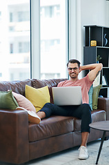 Image showing Im staying put but my websites taking off. a young man using a laptop while relaxing on a sofa.