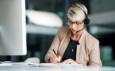 Image showing Ill be sure to follow-up on that. a young businesswoman wearing a headset while writing notes in an office.