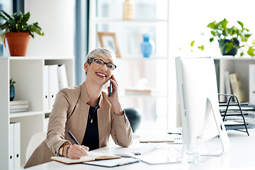 Image showing Shes always willing to go the extra mile for her clients. a young businesswoman writing notes while talking on a cellphone in an office.