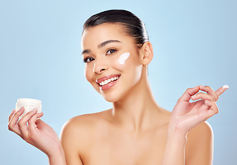 Image showing Sunscreen and water are your skins best friend. Studio portrait of an attractive young woman applying moisturiser on her face against a blue background.