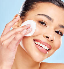 Image showing Following all the steps in her skincare routine. Studio portrait of an attractive young woman using a cotton pad on her face against a blue background.