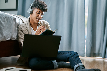 Image showing Stay at home, slay your goals. a young man writing in a notebook and using a laptop while listening to music at home.