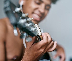 Image showing Strike the chords that keep you smiling. a young man using earbuds while playing the guitar at home.