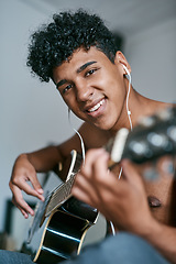 Image showing Staying at home Why not learn a new skill. a young man using earbuds while playing the guitar at home.