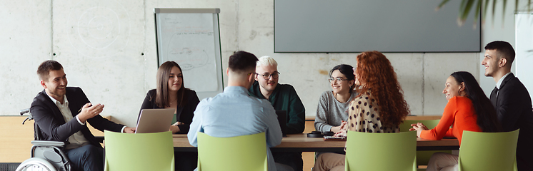 Image showing Wide crop photo of a diverse group of business professionals, including an person with a disability, gathered at a modern office for a productive and inclusive meeting.