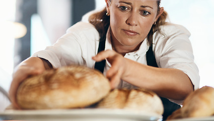 Image showing Freshly baked bread coming right up. a mature woman putting a selection of freshly baked breads on display in her bakery.