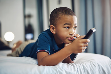 Image showing Mom says I can only watch educational shows. a young boy using a remote control while lying on his bed.