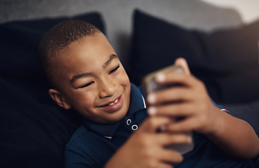 Image showing I love playing games on my moms cellphone. a young boy using a cellphone while lying on his bed.