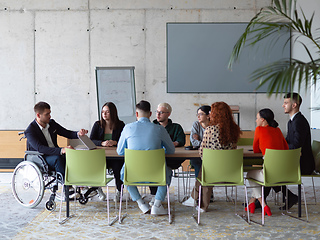 Image showing A diverse group of business professionals, including an person with a disability, gathered at a modern office for a productive and inclusive meeting.