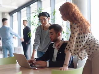 Image showing A businessman engaging in a discussion about sales statistics with his two female colleagues while they examine the data on a laptop in a modern office setting