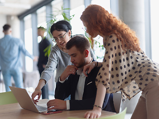 Image showing A businessman engaging in a discussion about sales statistics with his two female colleagues while they examine the data on a laptop in a modern office setting