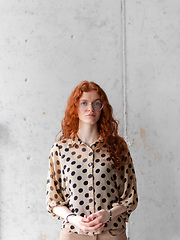 Image showing A young entrepreneur with captivating orange hair is striking a confident pose in front of a stylish gray wall.