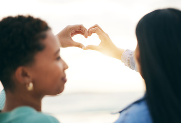 Image showing Love, beach and lesbian couple with heart hands from back at sunset, summer holiday adventure or date together. Lgbt women, bonding and ocean vacation with romance, pride and happy partner in nature.