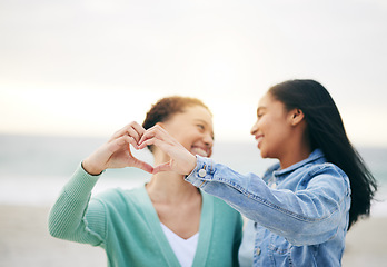 Image showing Love, ocean and lesbian couple with heart hands on summer holiday adventure or sunset date together. Lgbt women, bonding and relax on ocean vacation with romance, pride and happy partner in nature.