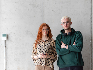 Image showing A blonde man and a woman with orange hair standing together, their arms crossed, posing confidently in front of a gray wall, exuding a sense of style and professionalism.