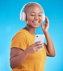 Image showing Woman, phone and headphones for music, listening to audio and social media influencer on a blue background. Young african person on mobile, video streaming subscribe and radio or selfie in studio