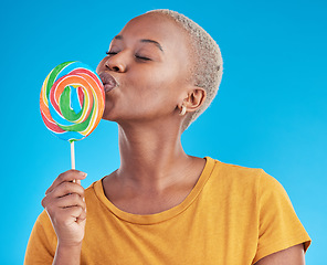 Image showing Lollipop, kiss and a woman with candy in studio for sweets, rainbow and creative advertising. Happy and funny black female person isolated on a blue background with love of sugar, freedom and color