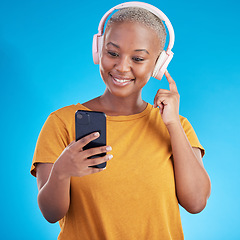Image showing Woman, headphones and phone listening to music, audio streaming service and social media on a blue background. Young african person or influencer with electronics, techno or radio on mobile in studio