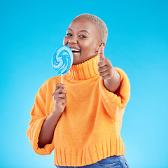 Image showing Thumbs up, lollipop and black woman in portrait with candy in studio isolated on a blue background. African person, happy face and sweets, dessert and sugar food with like hand sign for excellence