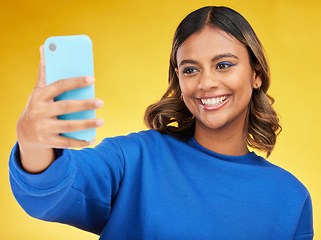 Image showing Selfie, social media and smile with a woman on a yellow background in studio posing for a profile picture. Face, photograph and a happy young influencer indoor to update a status on her timeline