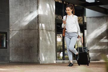 Image showing Phone, travel and luggage with a business woman walking in an airport parking lot outdoor in the city. Mobile, suitcase and commute with a young female employee on an international trip for work