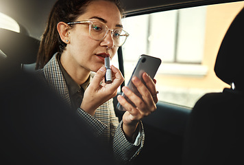 Image showing Phone, lipstick and a business woman in a car to travel in the city for work while multitasking. Face, mobile and makeup with a young female employee in a taxi or cab as a passenger for transport