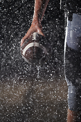 Image showing Close up of American Football Athlete Warrior Standing on a Field focus on his Helmet and Ready to Play. Player Preparing to Run, Attack and Score Touchdown. Rainy Night with Dramatic lens flare